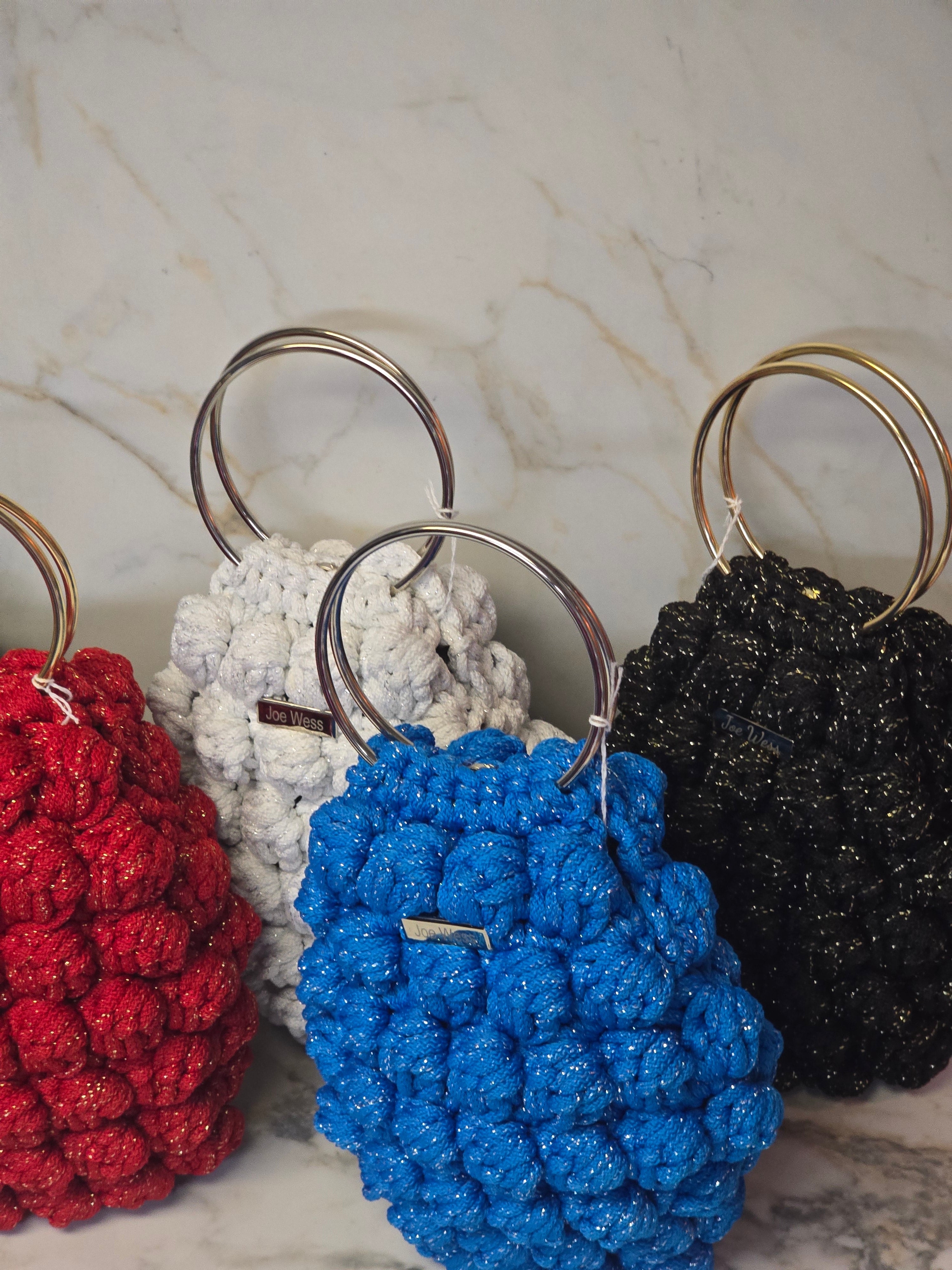 Four handcrafted crochet purses in white, red, blue, and black, each showcasing detailed stitching and a classic, stylish design.